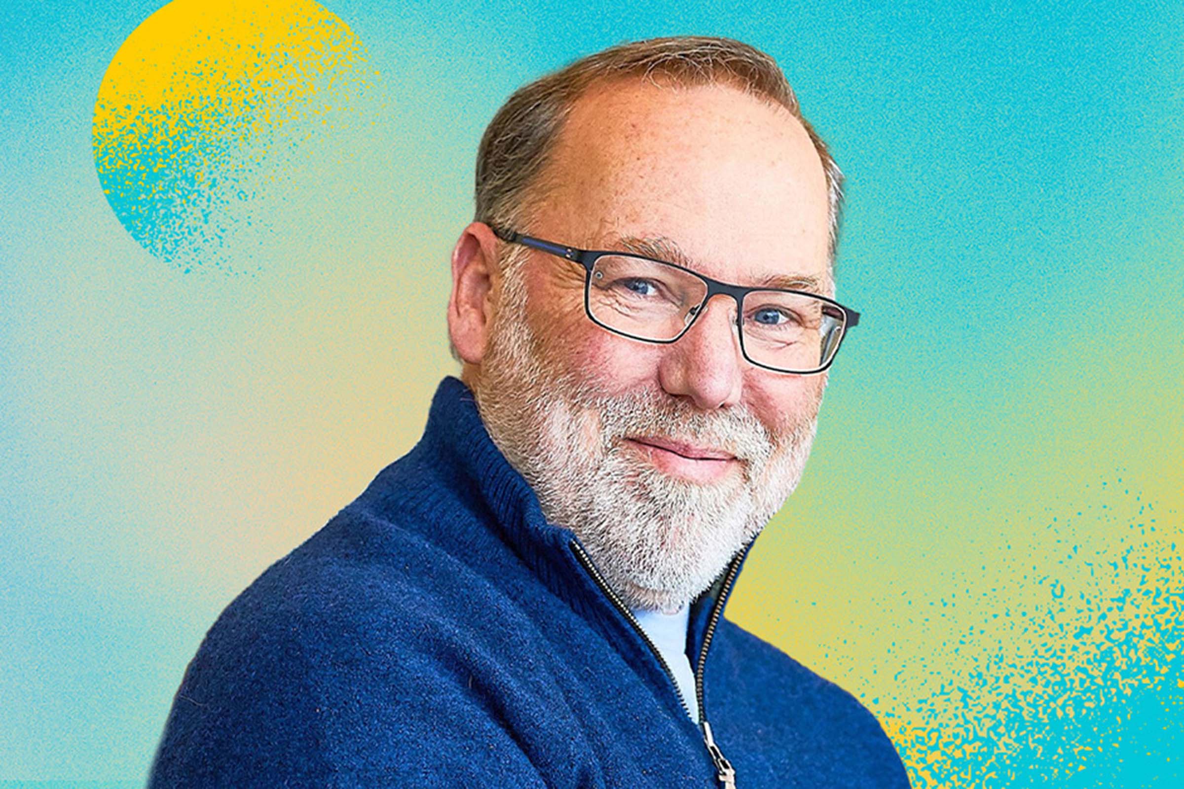 A person with white beard and glasses smiles against blue and yellow background.